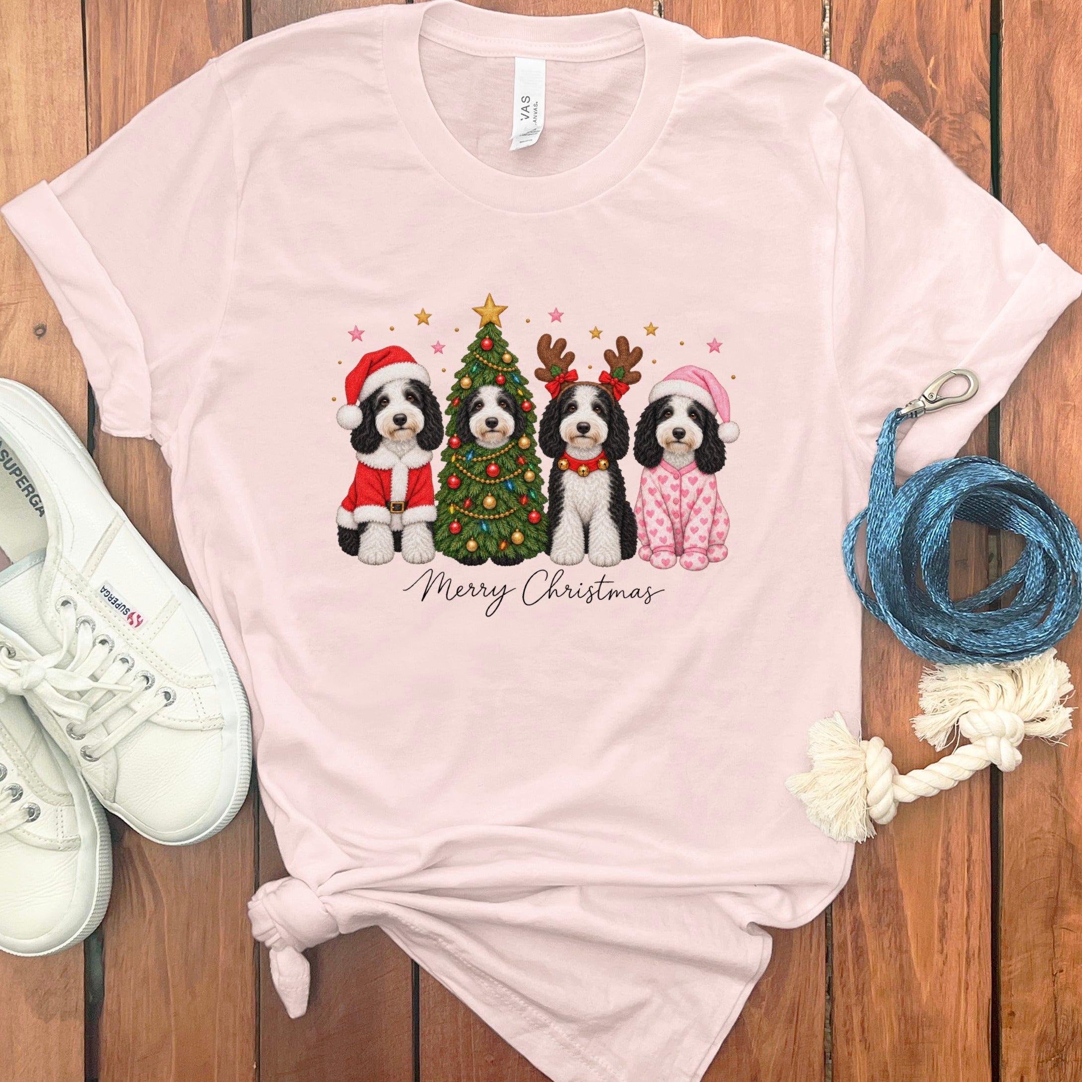 Light pink t-shirt featuring four dogs in Christmas costumes around a decorated tree with Merry Christmas text.