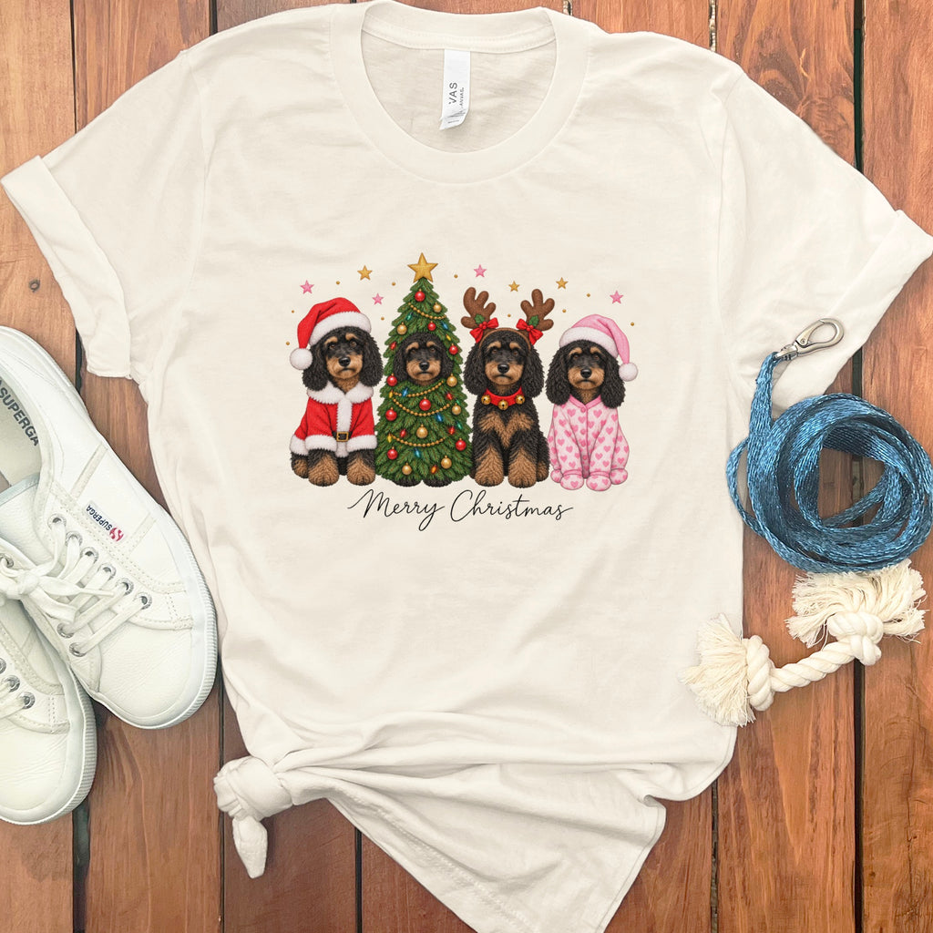 A white t-shirt featuring a graphic of four doodle dogs celebrating Christmas with a tree and the text "Merry Christmas."