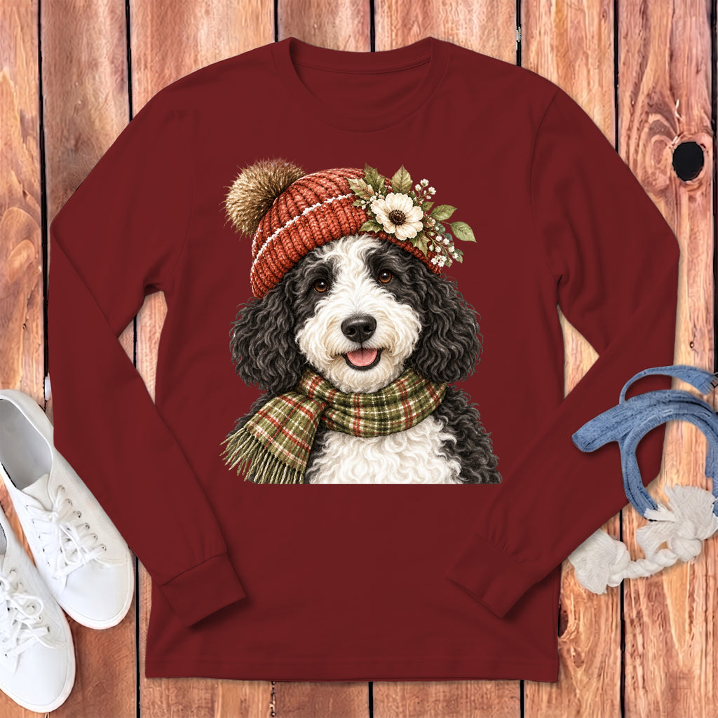 Bernedoodle dog wearing a festive hat and scarf on a maroon shirt.