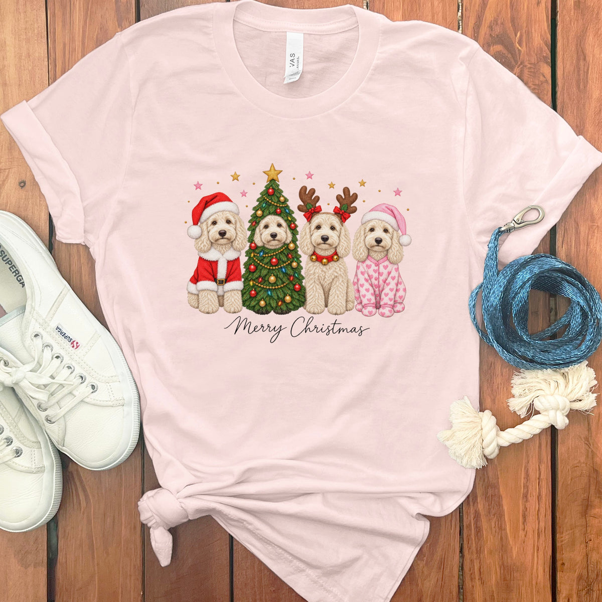 Light pink t-shirt featuring a graphic of four doodle dogs celebrating Christmas with the text Merry Christmas.
