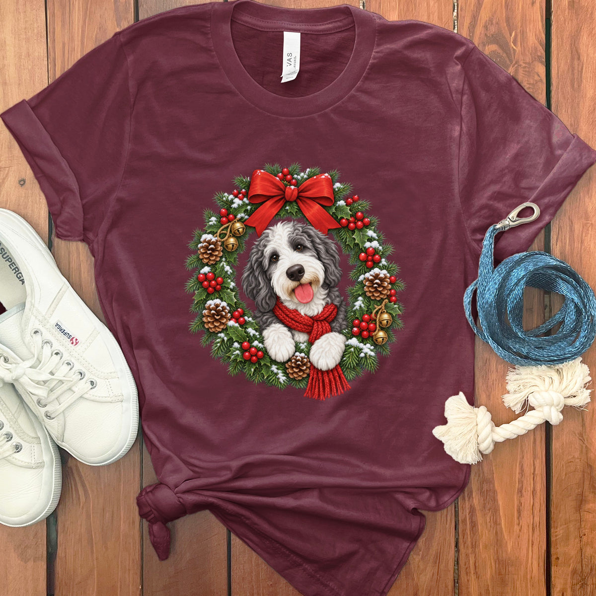 Maroon t-shirt featuring a doodle dog in a Christmas wreath with a red bow and scarf.