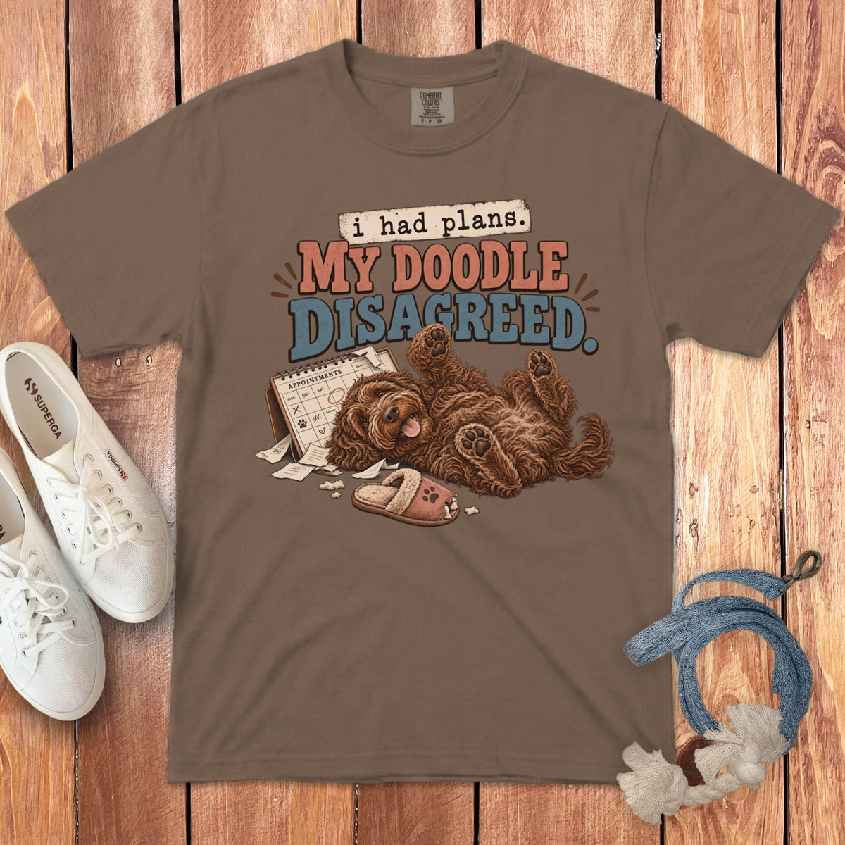 A brown t-shirt featuring a playful illustration of a doodle dog lying on its back amidst ripped appointment planner pages.