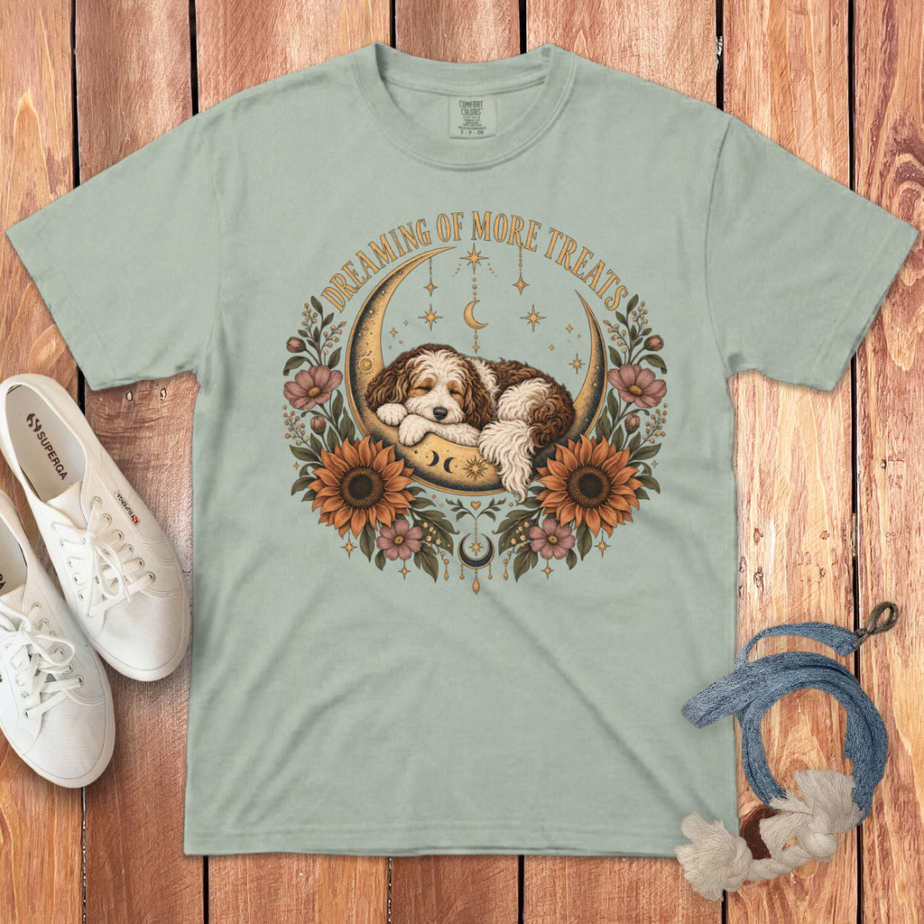 Light green t-shirt with a graphic of a sleeping puppy on a crescent moon, surrounded by flowers and the text Dreaming of More Treats.