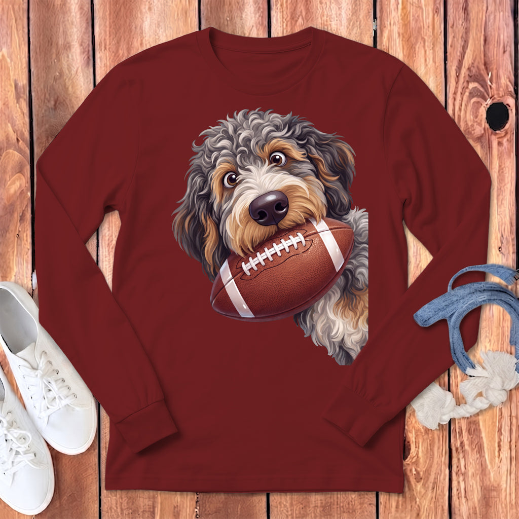 Maroon long-sleeved t-shirt featuring a cartoon doodle dog holding a football in its mouth, laid on wood.