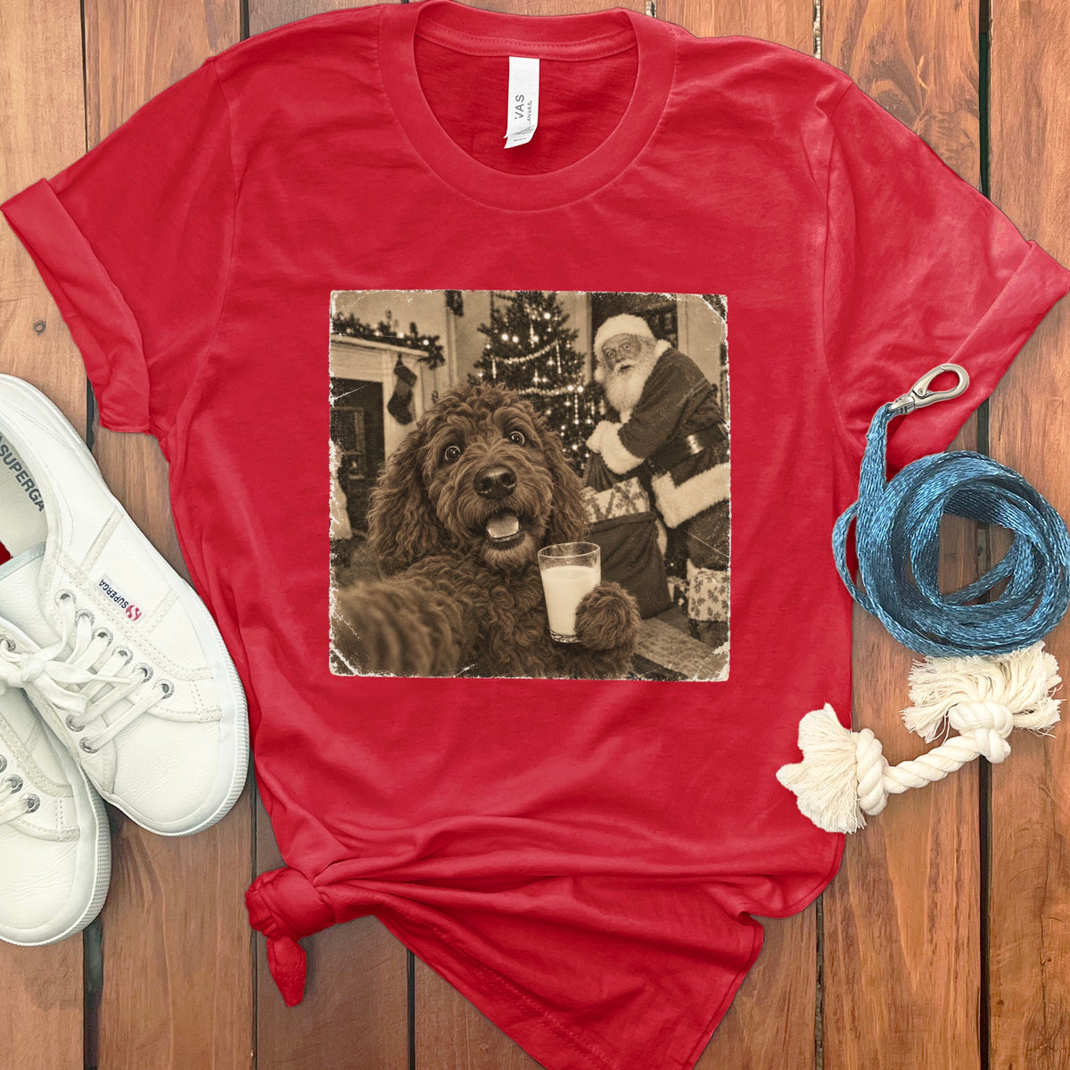 A red t-shirt with a graphic of a brown dog holding a glass of milk in front of Santa Claus.