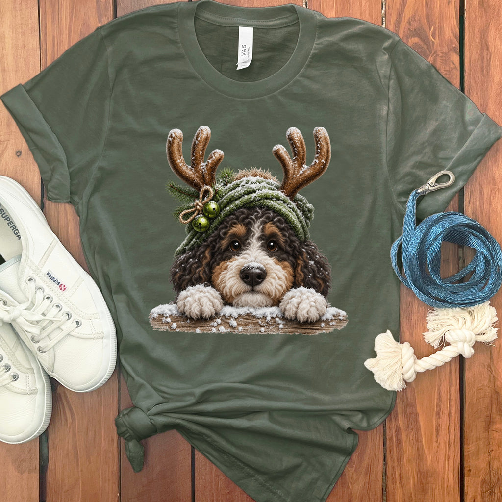 Bernedoodle wearing reindeer antlers and winter hat, with snow on wooden fence.