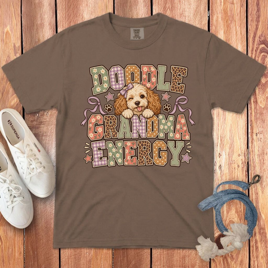 Brown t-shirt featuring a cartoon doodle dog and the text Doodle Grandma Energy laid flat on a wooden surface.