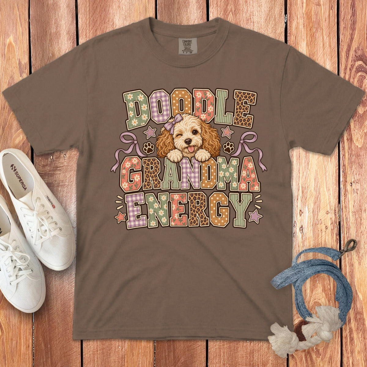 Brown t-shirt featuring a cartoon doodle dog and the text Doodle Grandma Energy laid flat on a wooden surface.