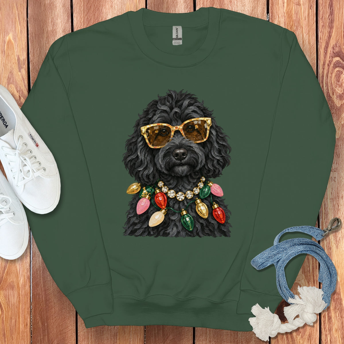 Black dog wearing sunglasses and Christmas lights on a green sweatshirt.