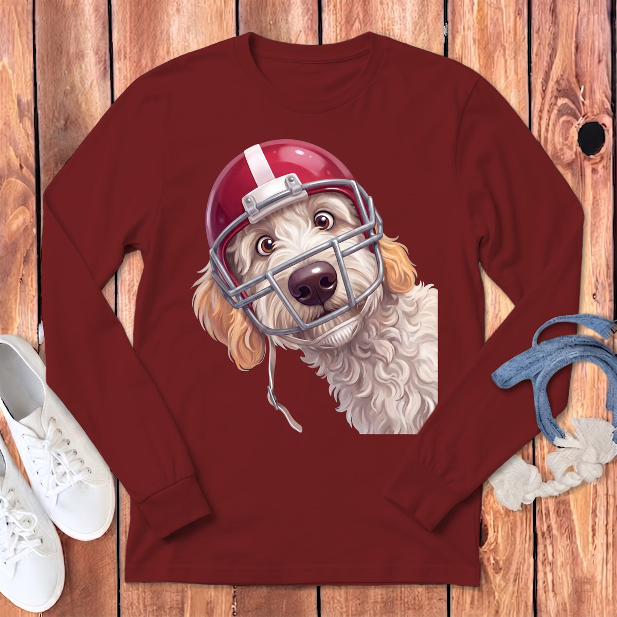Goldendoodle dog wearing a red and white football helmet on a maroon long-sleeve shirt.