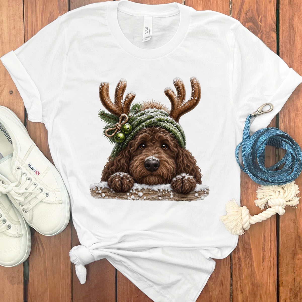 White t-shirt with a brown dog wearing antlers and a green hat with bells.