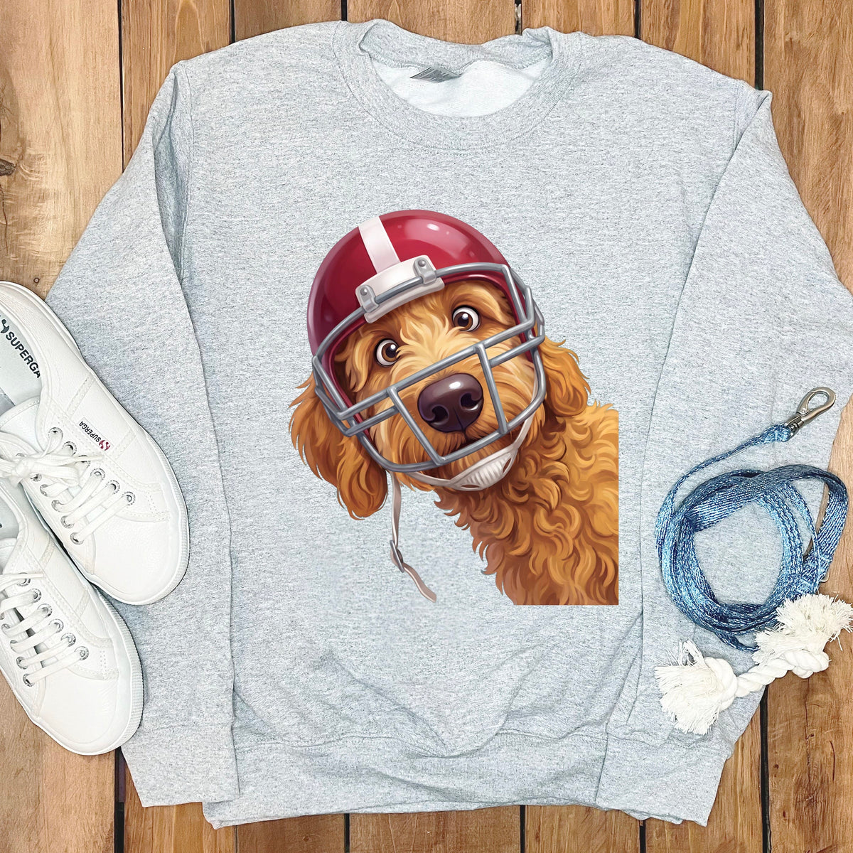 Goldendoodle dog wearing a red football helmet on a grey sweatshirt.