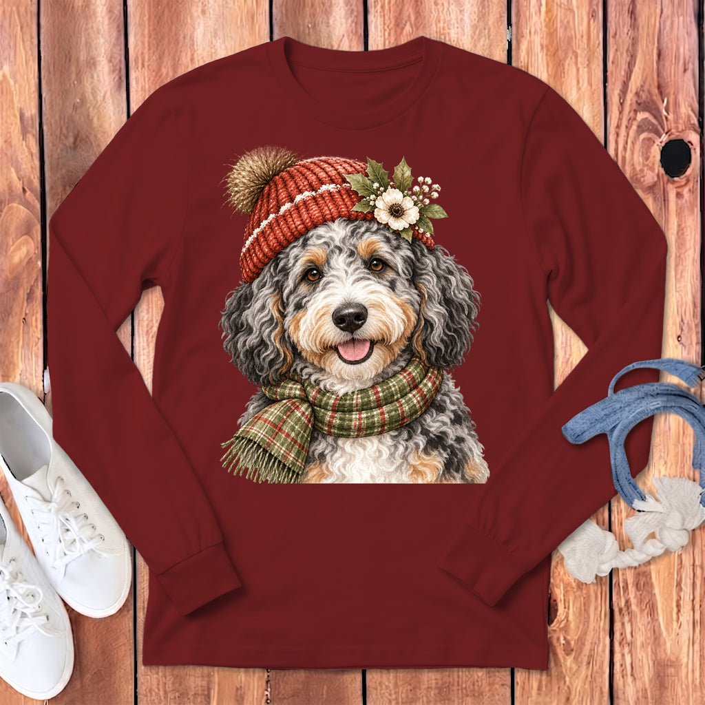 Bernedoodle dog wearing winter hat and scarf on maroon long-sleeved shirt.