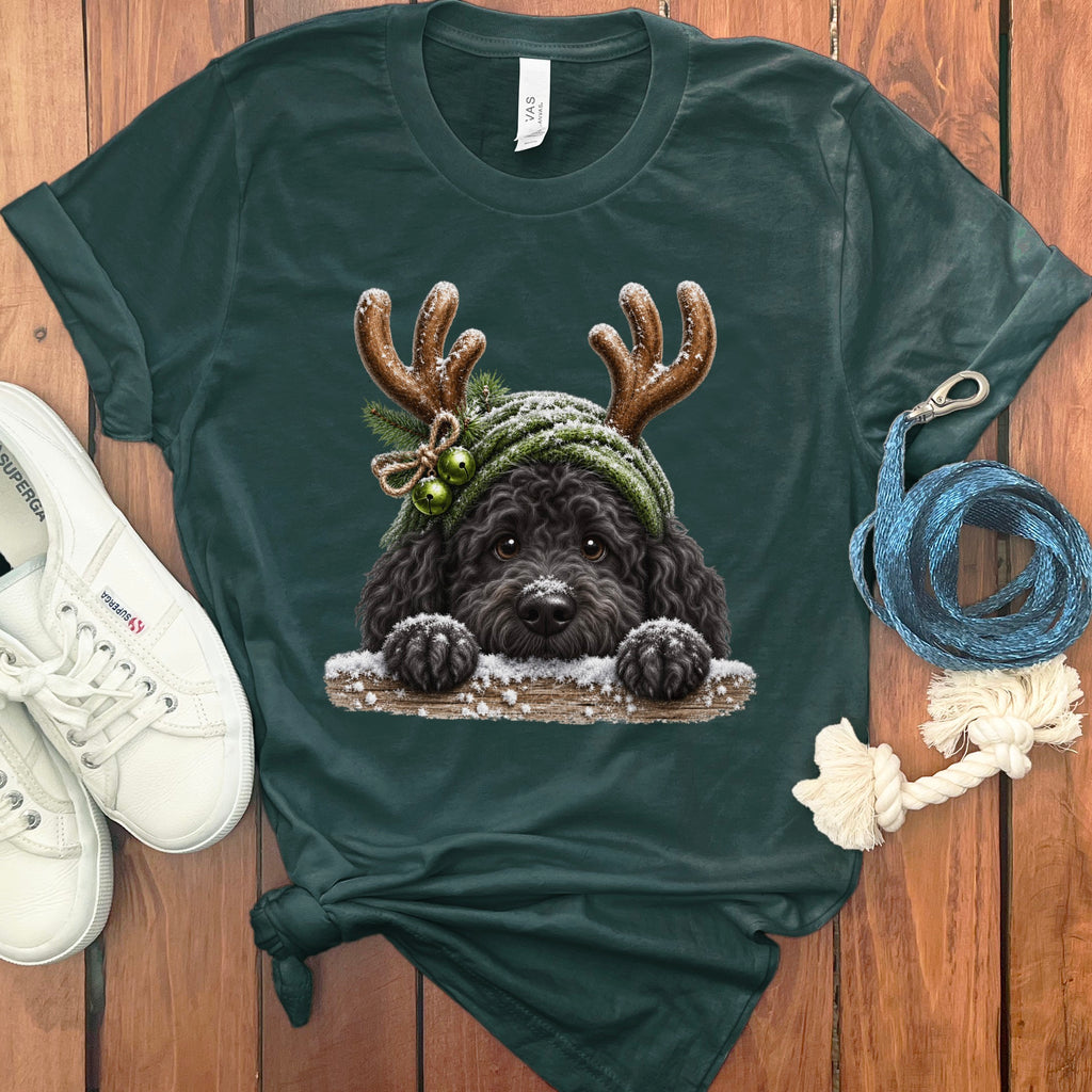 T-shirt featuring a black poodle wearing a green knitted hat with antlers, bells, and pine sprigs.