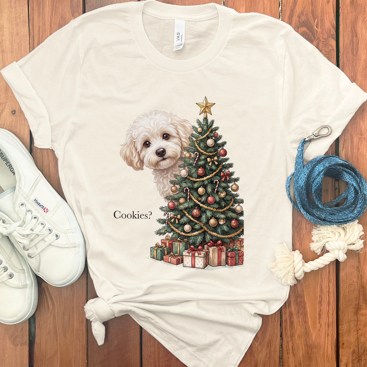 White t-shirt with a white fluffy dog peeking behind a decorated Christmas tree and presents.