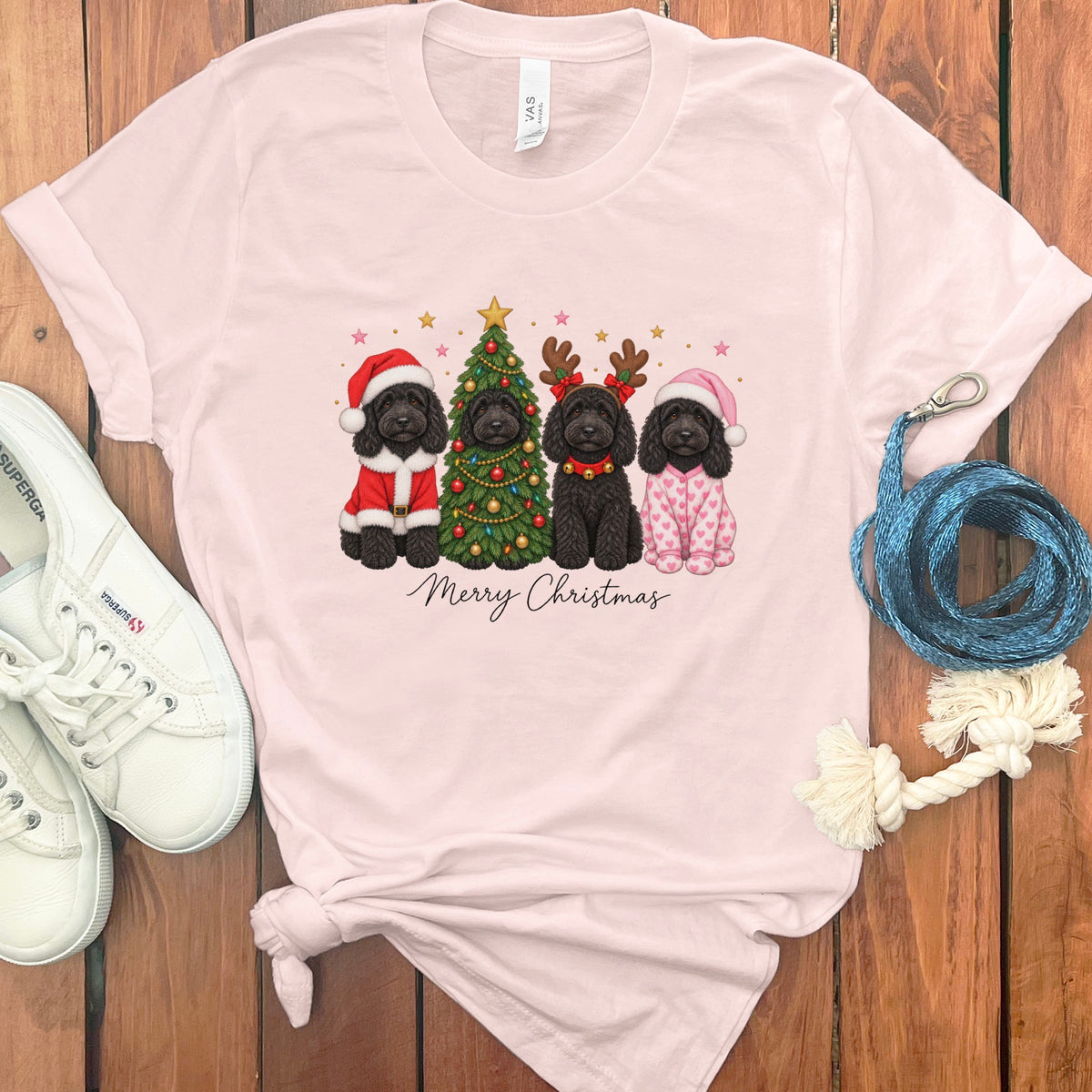 Light pink t-shirt featuring four black doodles in Christmas costumes, a decorated tree, and Merry Christmas text.