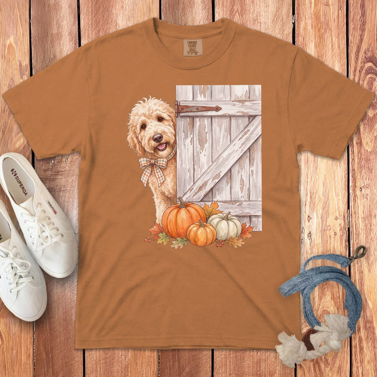 Orange t-shirt with a doodle peeking from behind a rustic barn door with pumpkins and leaves.