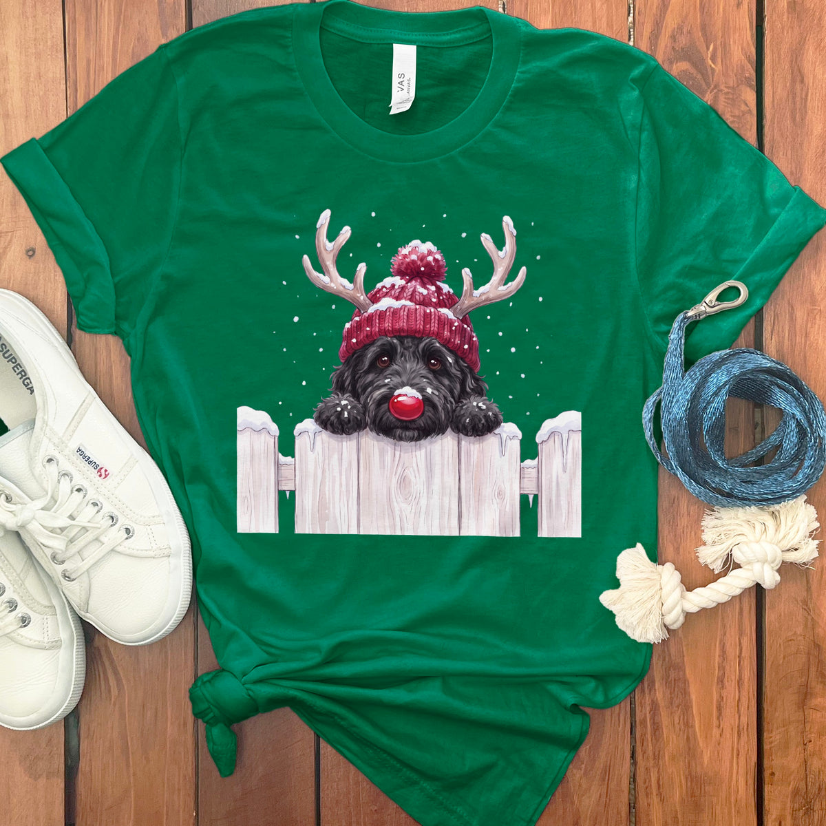 Green t-shirt with a black dog wearing a Santa hat and red nose over a fence.