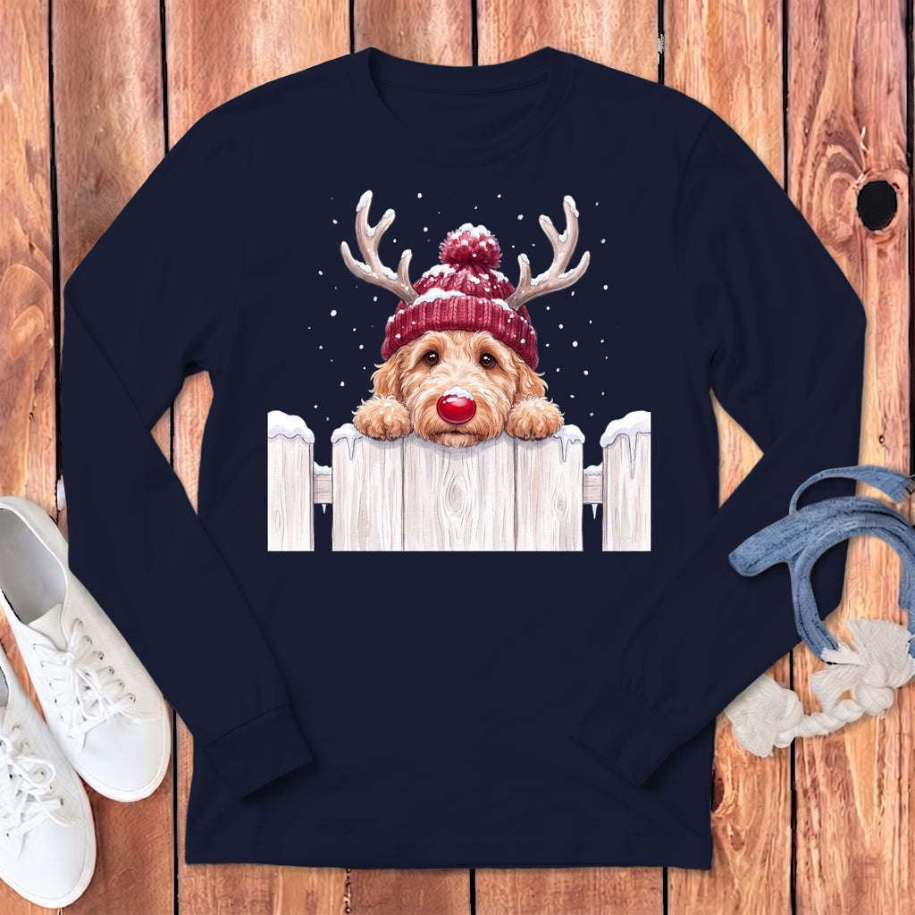 Goldendoodle dog in a red beanie with reindeer antlers peeking over a snowy fence.
