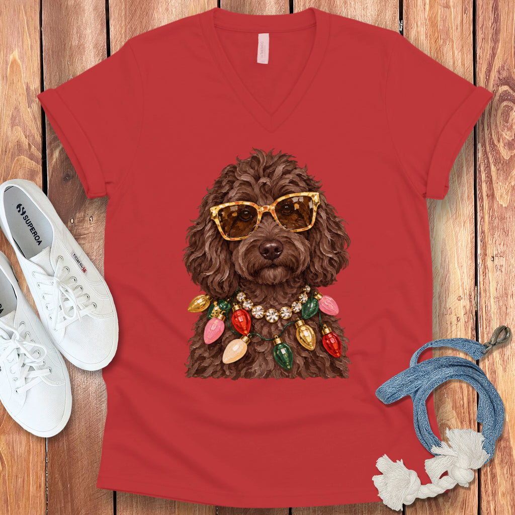 Brown poodle wearing sunglasses and a Christmas light necklace on a red shirt.