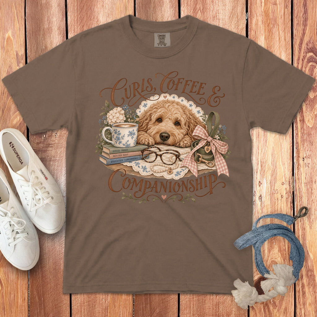 Brown t-shirt featuring a graphic of a Goldendoodle, books, a coffee mug, and text saying Curls Coffee and Companionship.