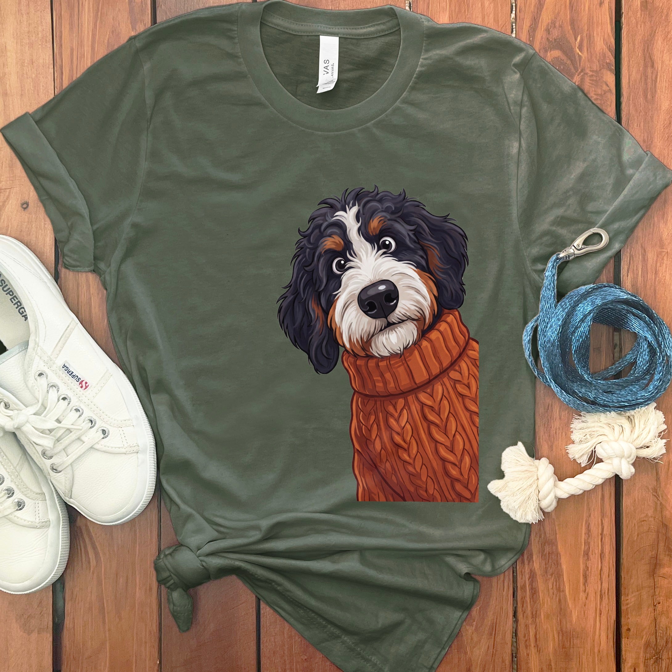 Green t-shirt with a drawing of a Bernese Mountain Dog wearing an orange knit sweater.