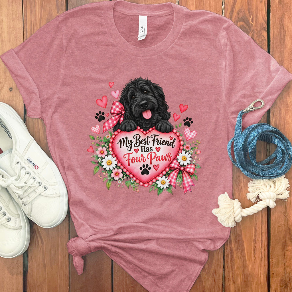 Heather pink t-shirt featuring a black dog illustration holding a heart that reads My Best Friend Has Four Paws, surrounded by flowers, hearts, and paw prints, displayed with white sneakers and a blue leash on a wooden background.