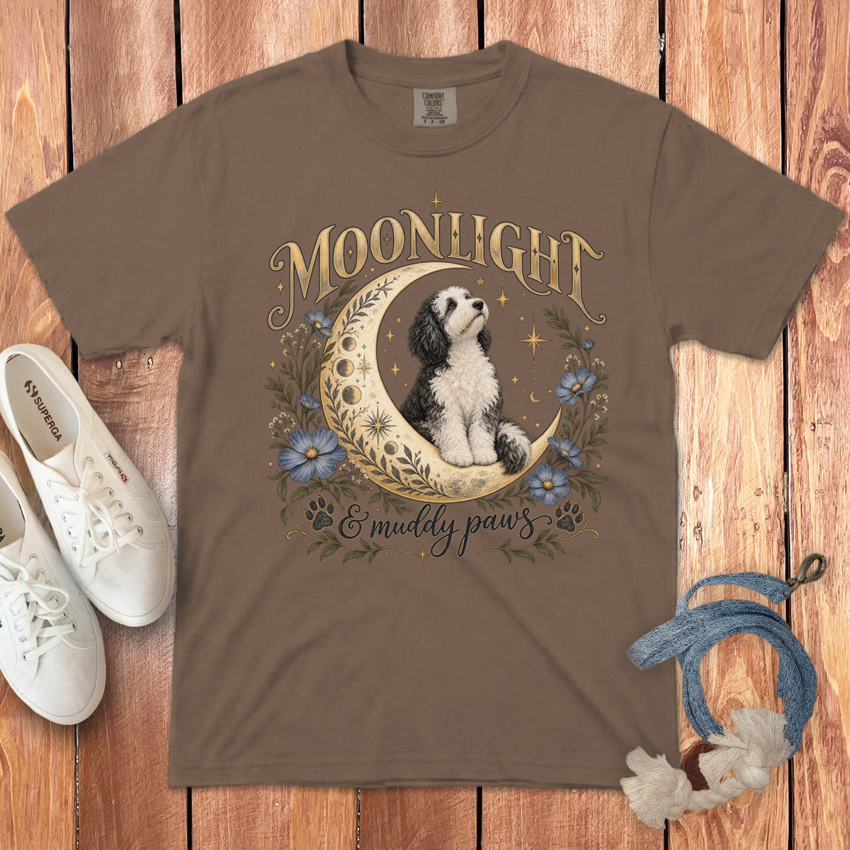 Brown t-shirt featuring a black and white doodle dog sitting on a crescent moon with floral elements.