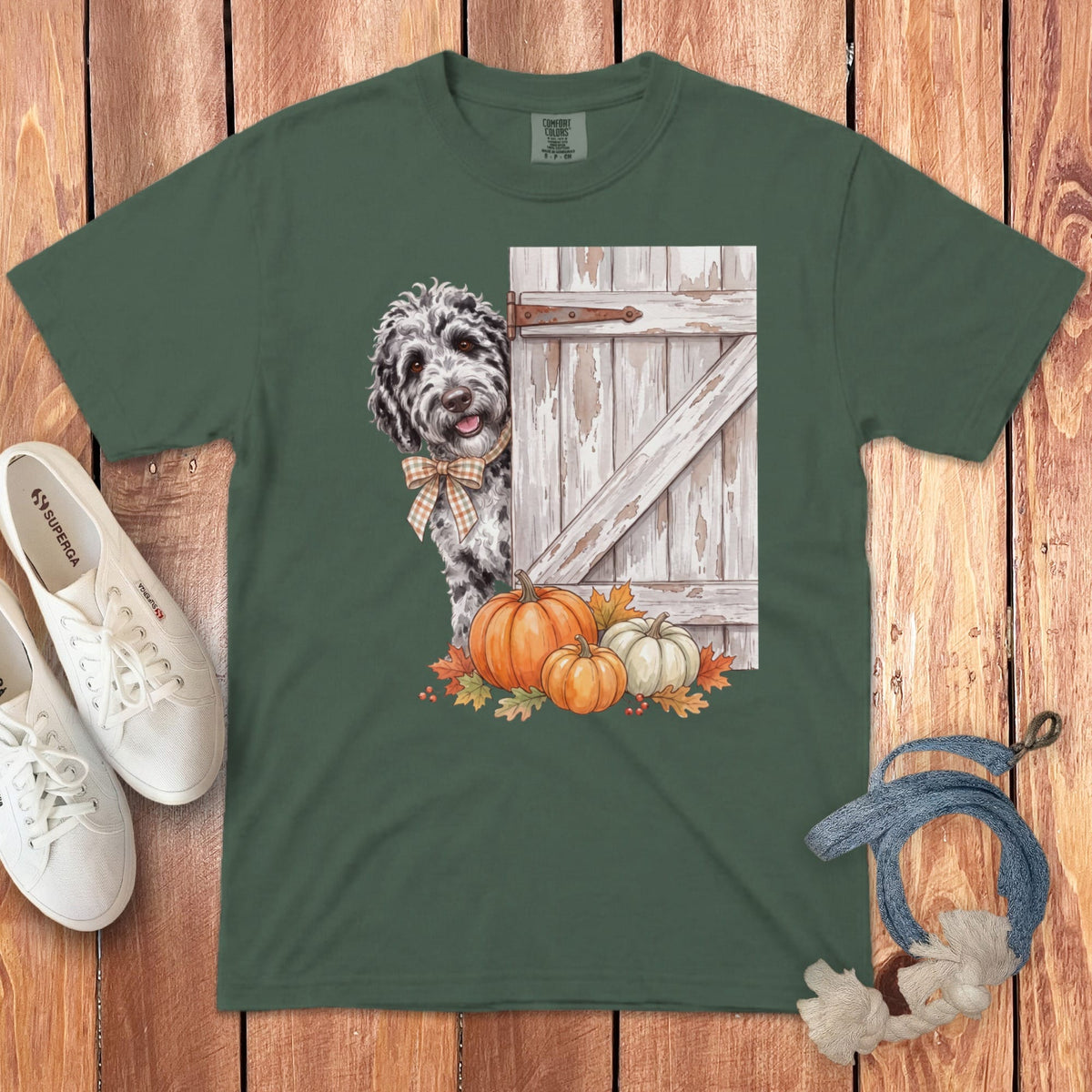 Green t-shirt with dog peeking from behind a barn door with pumpkins and autumn leaves.