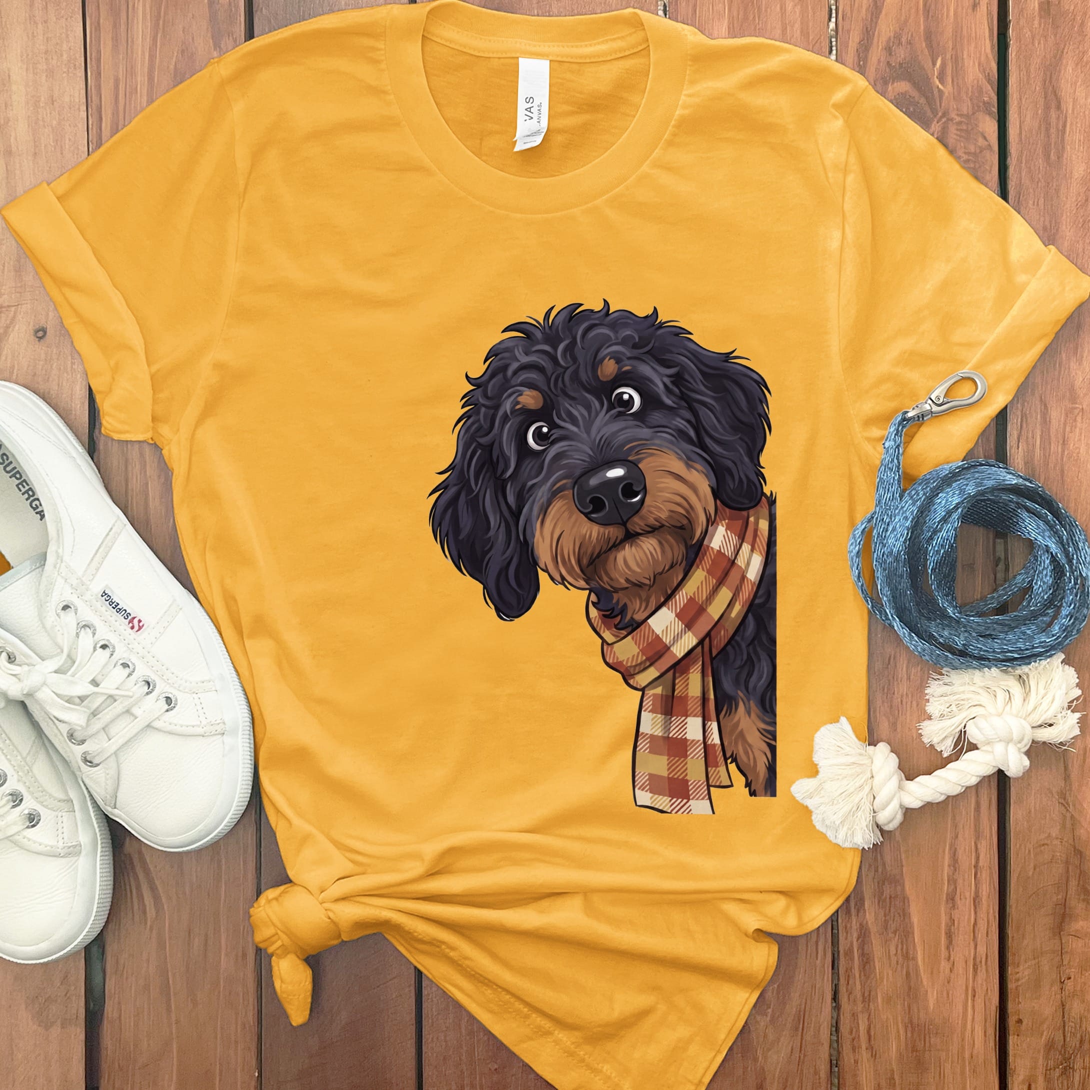 A doodle dog wearing a plaid scarf peeks from the side of a yellow t-shirt.
