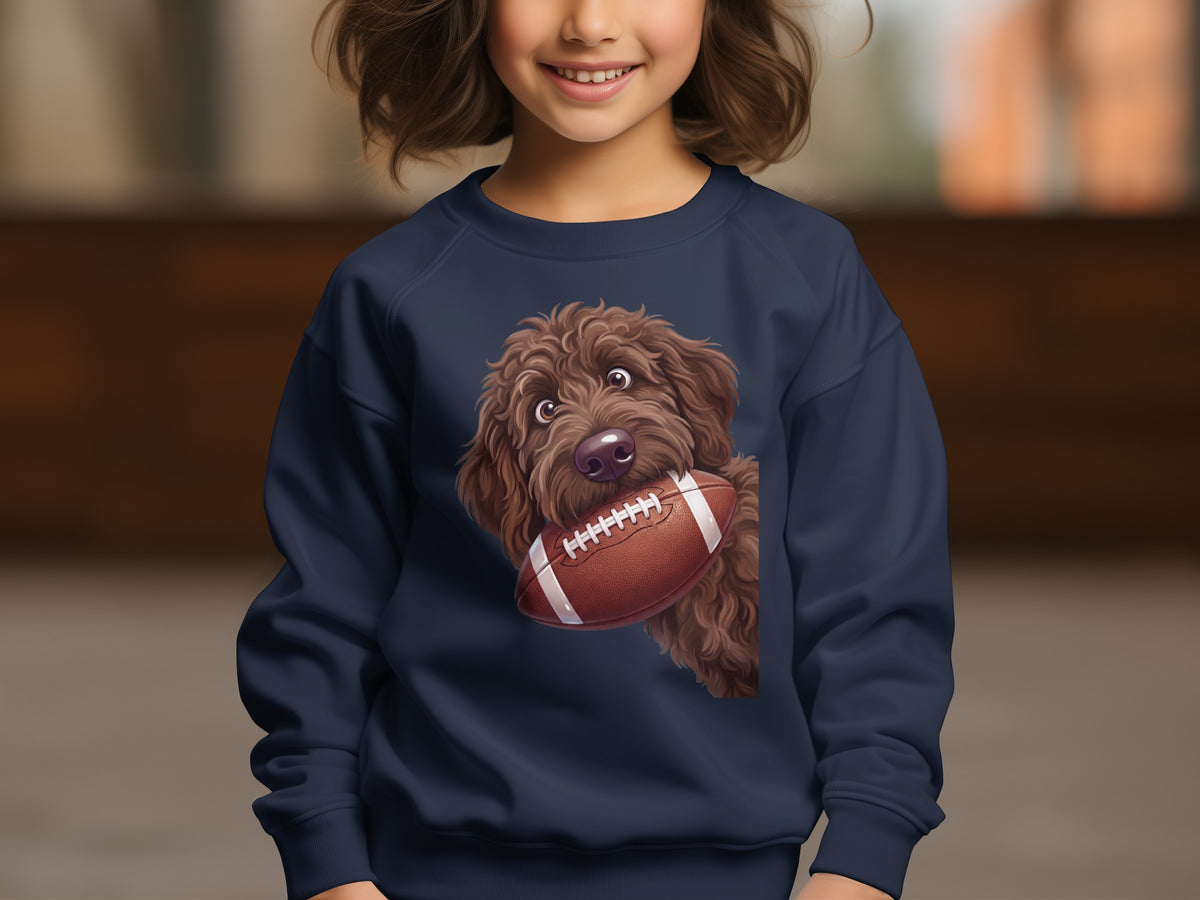 Brown doodle dog holding an American football graphic on a navy sweatshirt.