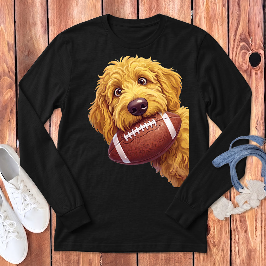 Golden doodle dog with a football in its mouth on a black long-sleeve shirt.