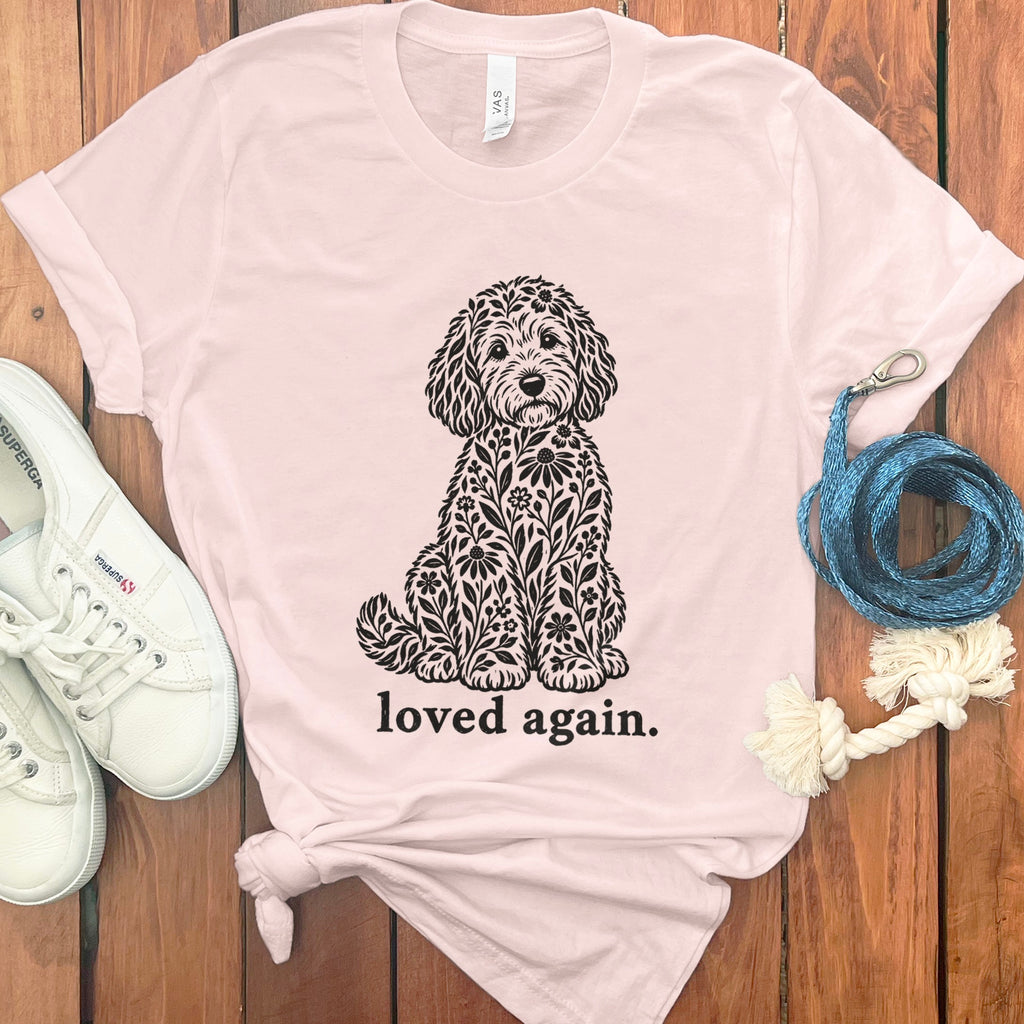 Pink t-shirt with a black floral dog illustration and text "loved again."