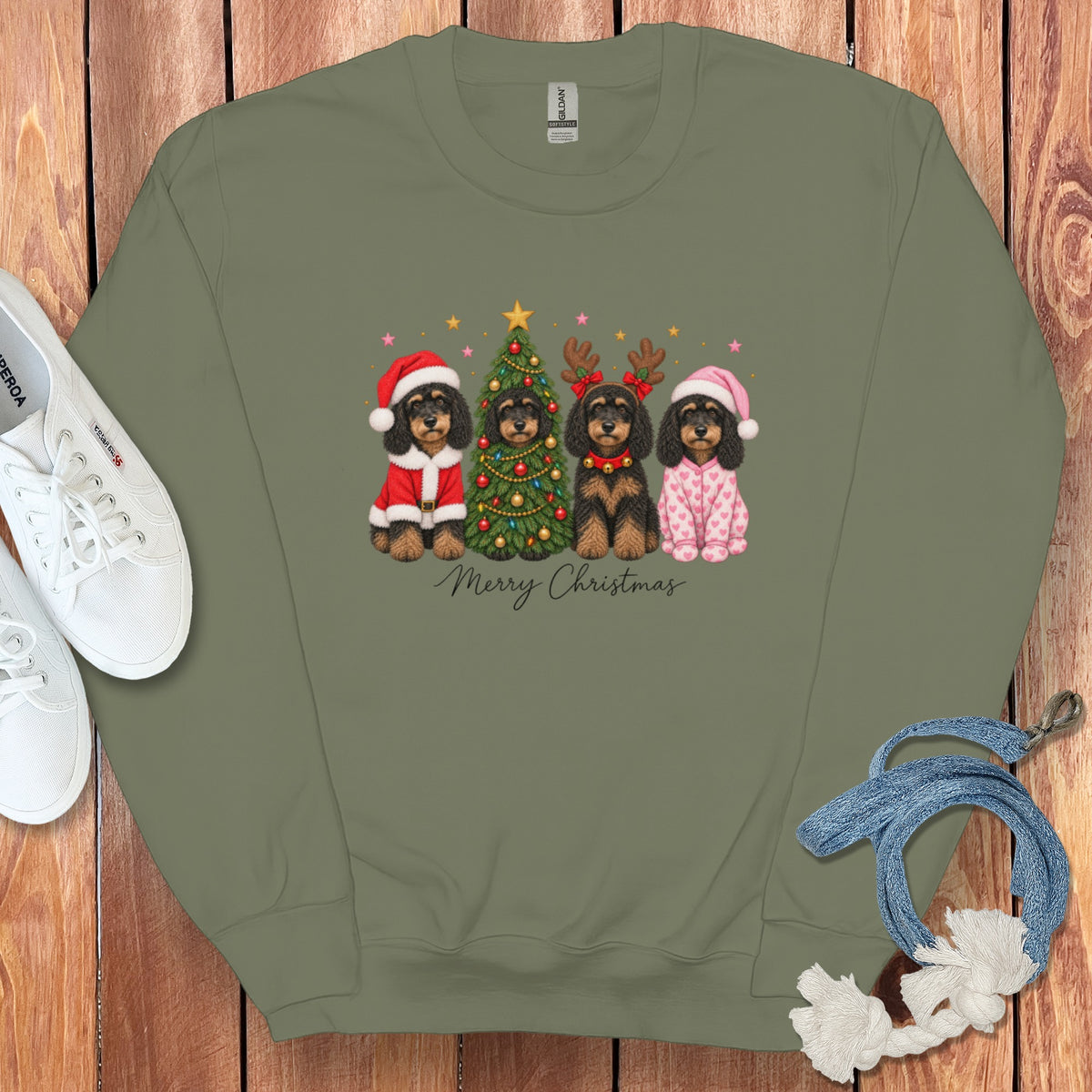 An olive green crewneck sweatshirt featuring a graphic of four dogs celebrating Christmas with a tree and the text Merry Christmas.