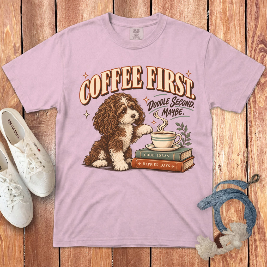 Pink t-shirt with a graphic of a brown doodle dog, coffee cup, books, and text reading COFFEE FIRST.