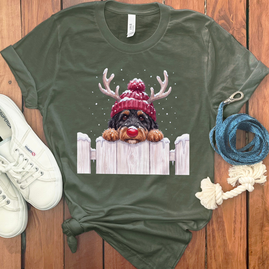 Green t-shirt featuring a Bernedoodle dog wearing a red beanie and antlers over a white fence.