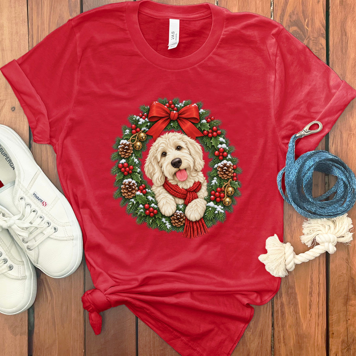 Red crewneck t-shirt featuring a Christmas wreath graphic with a fluffy dog, surrounded by white shoes and a blue leash.