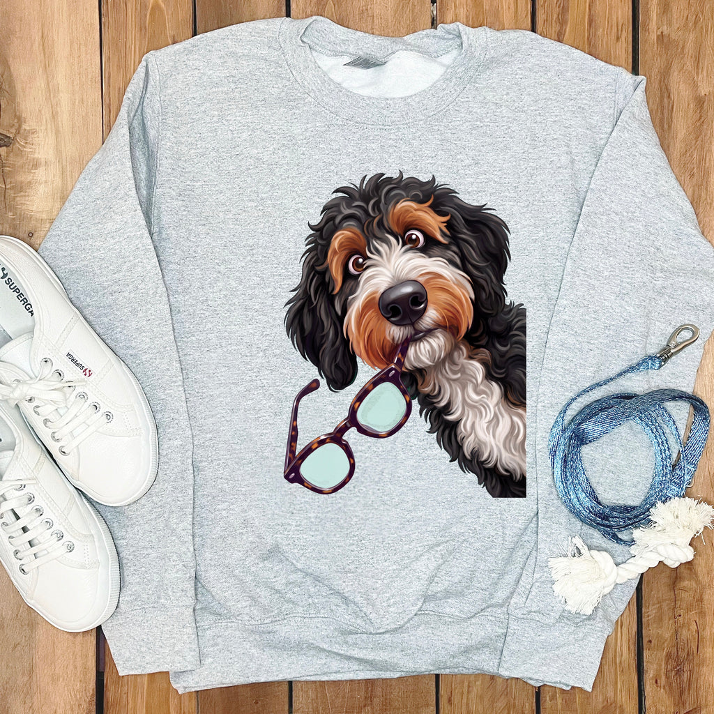 Light gray crewneck sweatshirt featuring a graphic of a Bernedoodle holding glasses, with white sneakers and a blue leash.