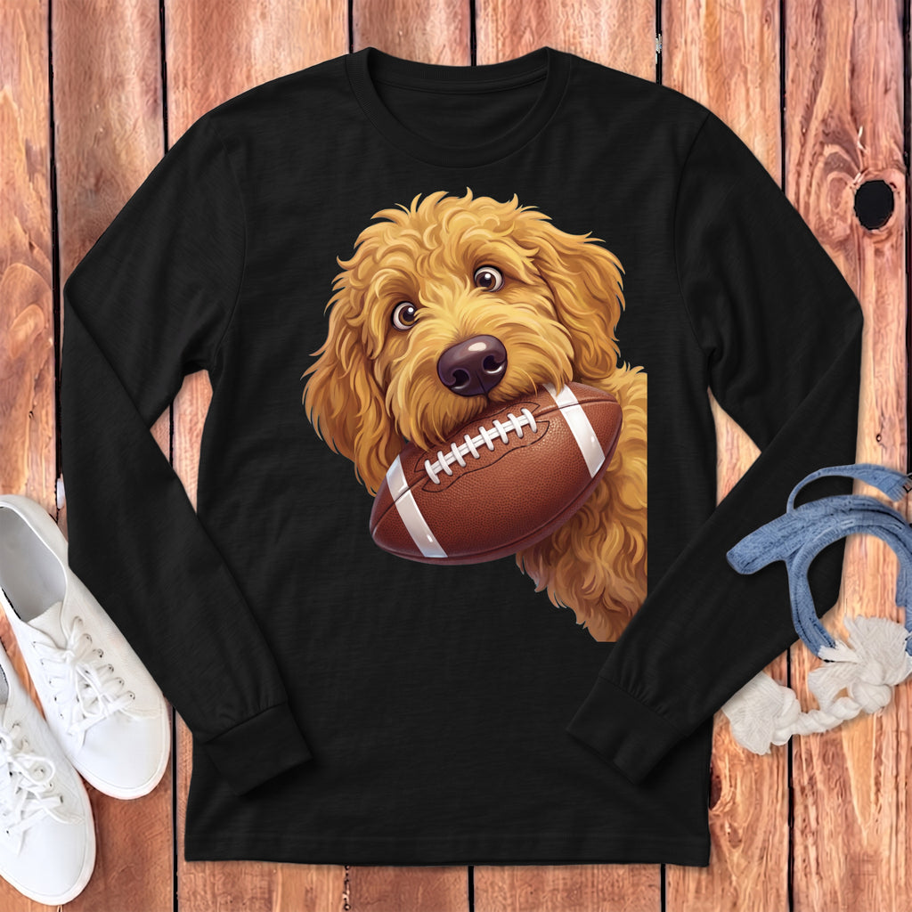 Golden doodle dog with brown football in mouth on black long-sleeve shirt.