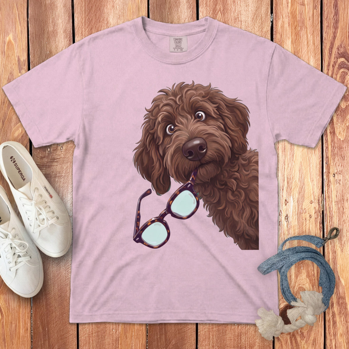 A light pink t-shirt featuring an illustration of a brown curly-haired dog holding glasses in its mouth.