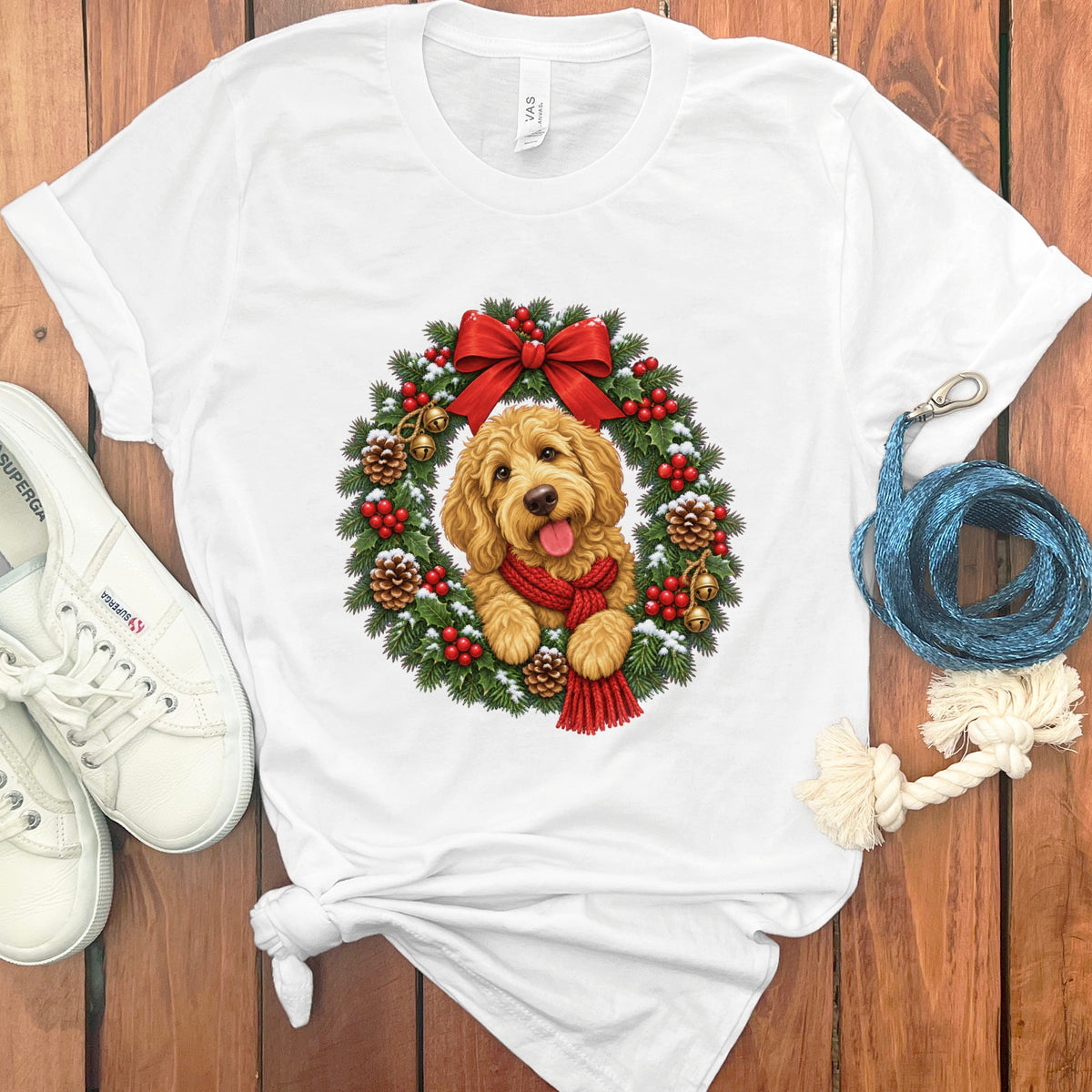 A white crewneck t-shirt featuring a golden doodle wearing a red scarf inside a Christmas wreath.