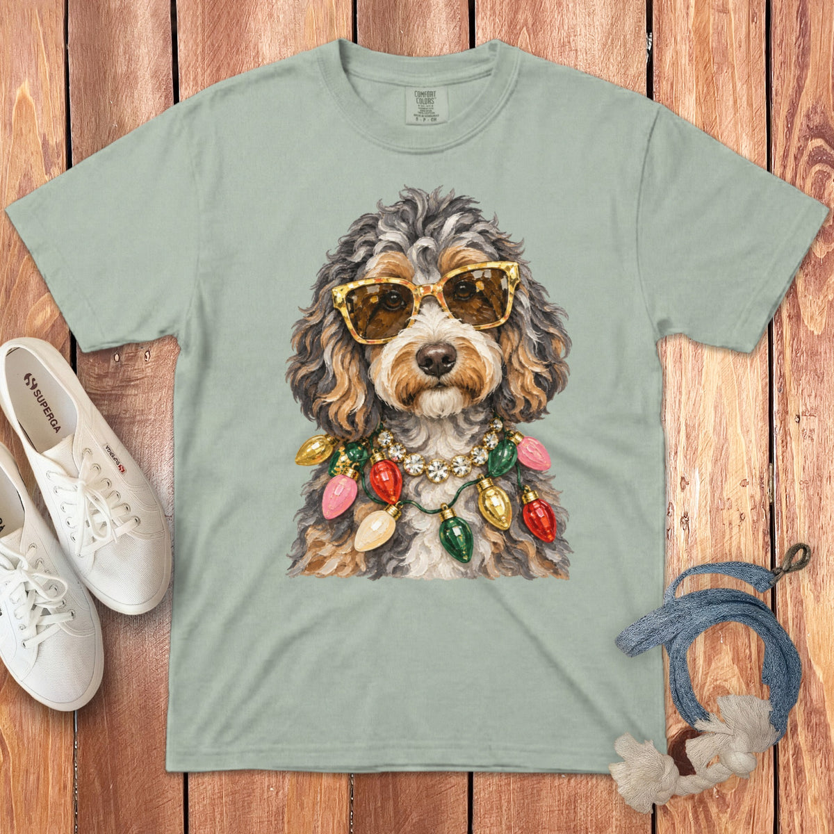 Dog with sunglasses and Christmas lights necklace on a sage green t-shirt.
