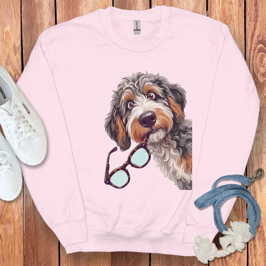 A pink crewneck sweatshirt features an illustrated doodle dog holding tortoise shell glasses in its mouth.