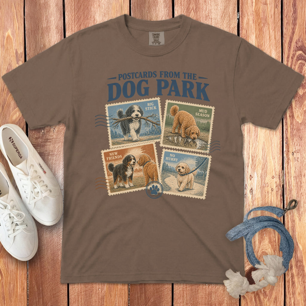 Brown t-shirt featuring graphic text Postcards from the Dog Park above four vintage-style dog postage stamp illustrations.