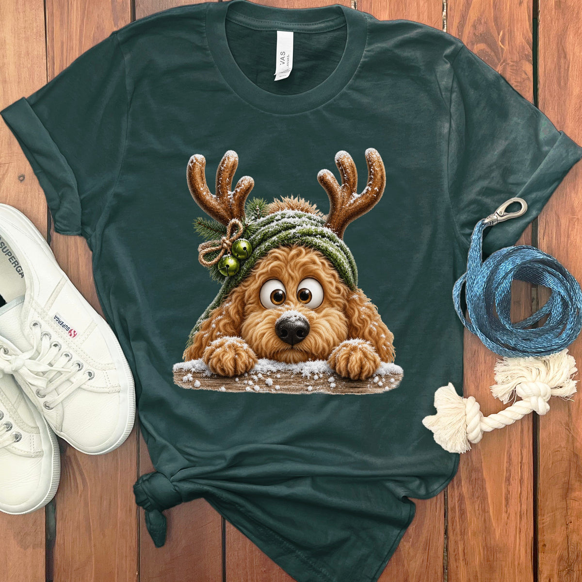 Dog with reindeer antlers and a green hat peeking over a snowy log.