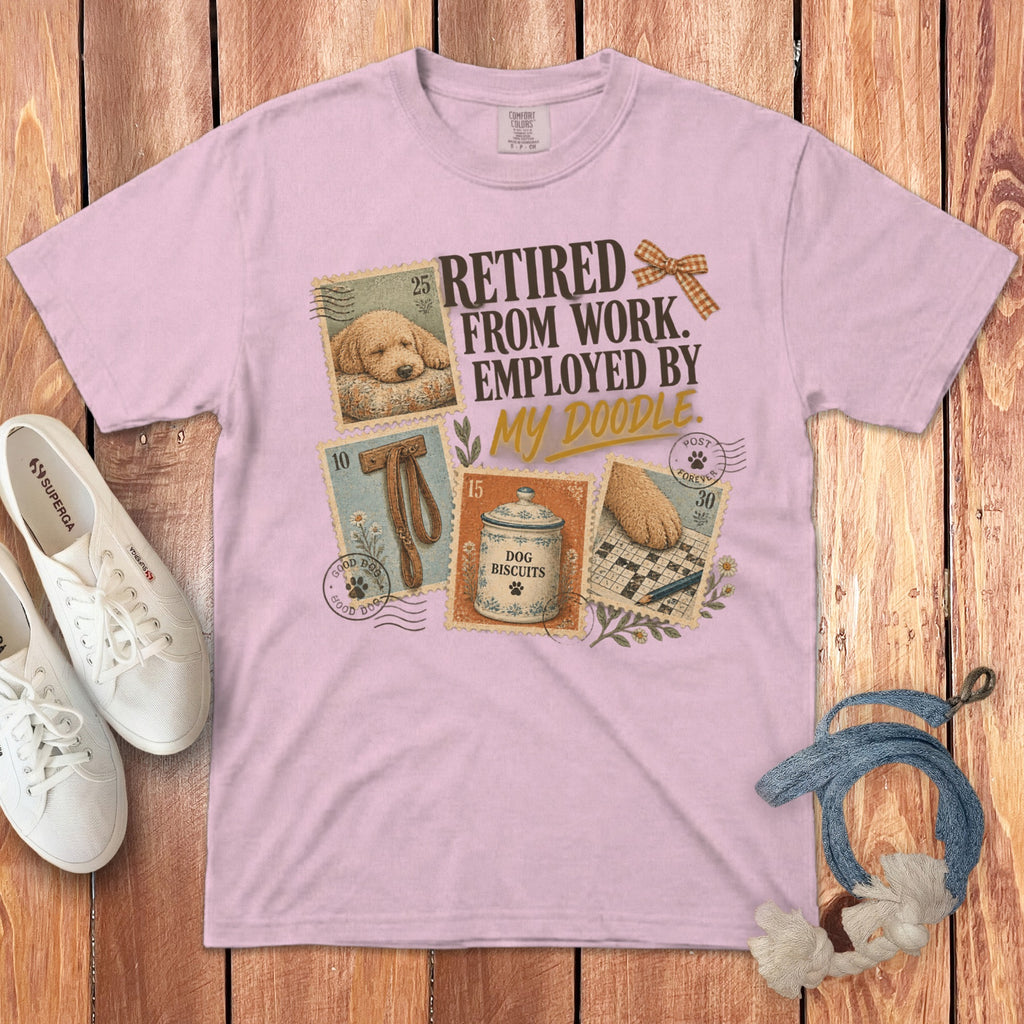 A light pink t-shirt with vintage postage stamp graphics featuring a doodle dog and the text Retired from work employed by my doodle.