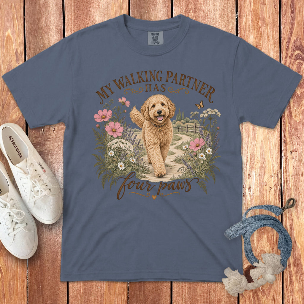 Slate blue t-shirt featuring a goldendoodle on a path surrounded by flowers, with the text "MY WALKING PARTNER HAS four paws".
