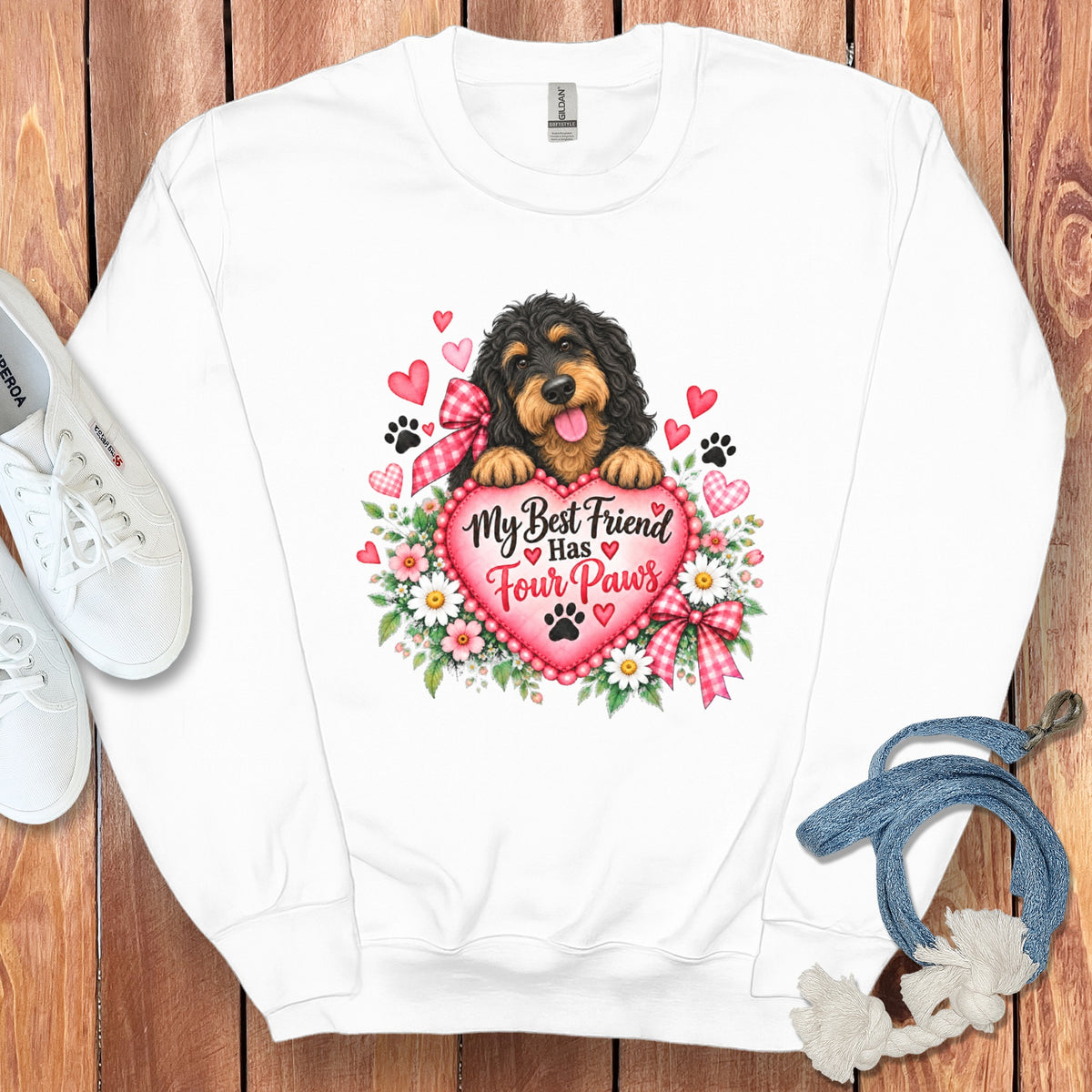 A white crewneck sweatshirt featuring a graphic of a Bernedoodle dog resting on a pink heart that says My Best Friend Has Four Paws, surrounded by flowers, gingham bows, and hearts.