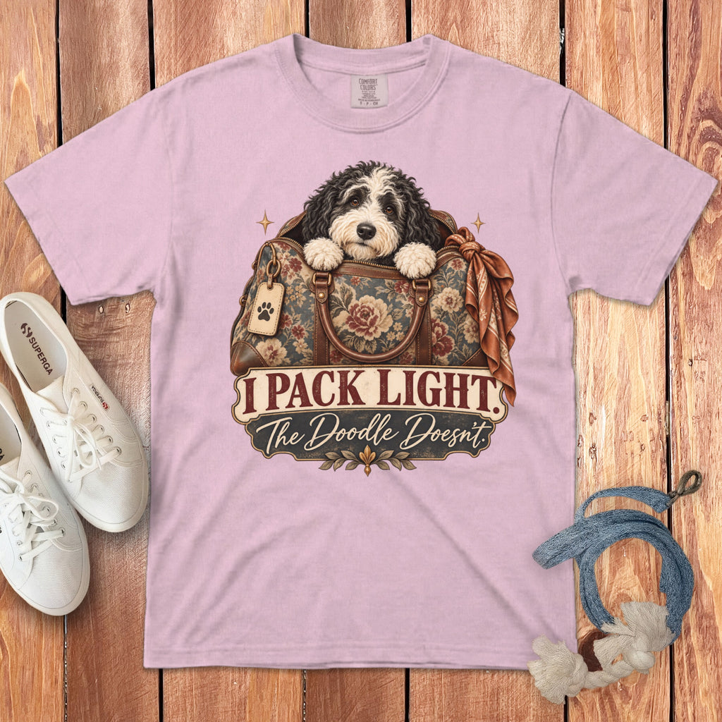 A pink t-shirt featuring a doodle dog in a floral travel bag with text reading I Pack Light The Doodle Doesnt.