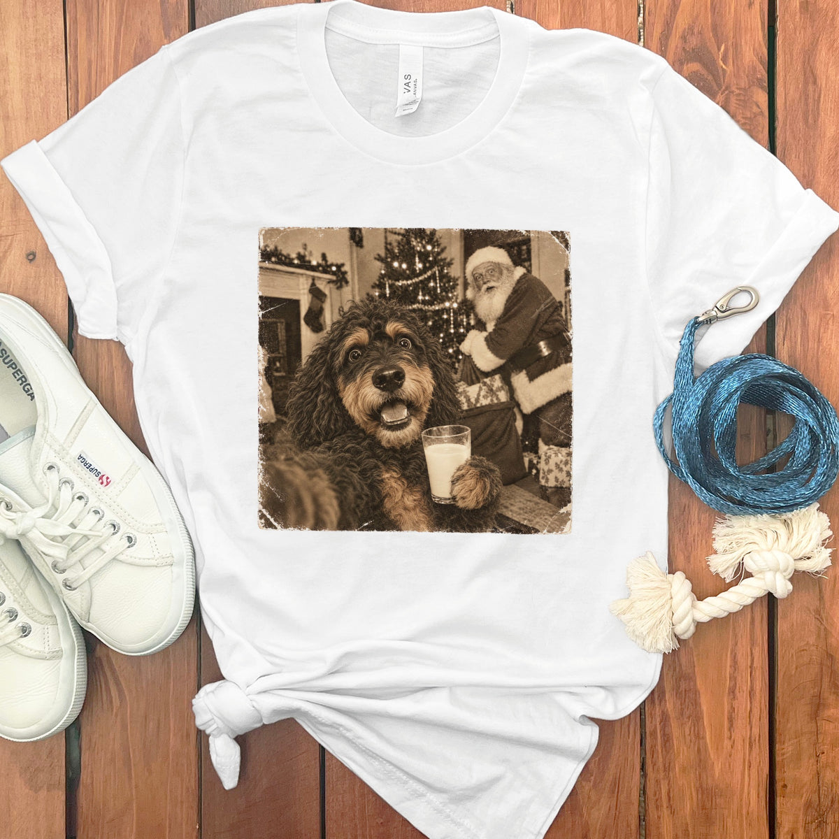 A white t-shirt featuring a sepia-toned graphic of a fluffy dog holding a glass of milk with Santa Claus in the background.